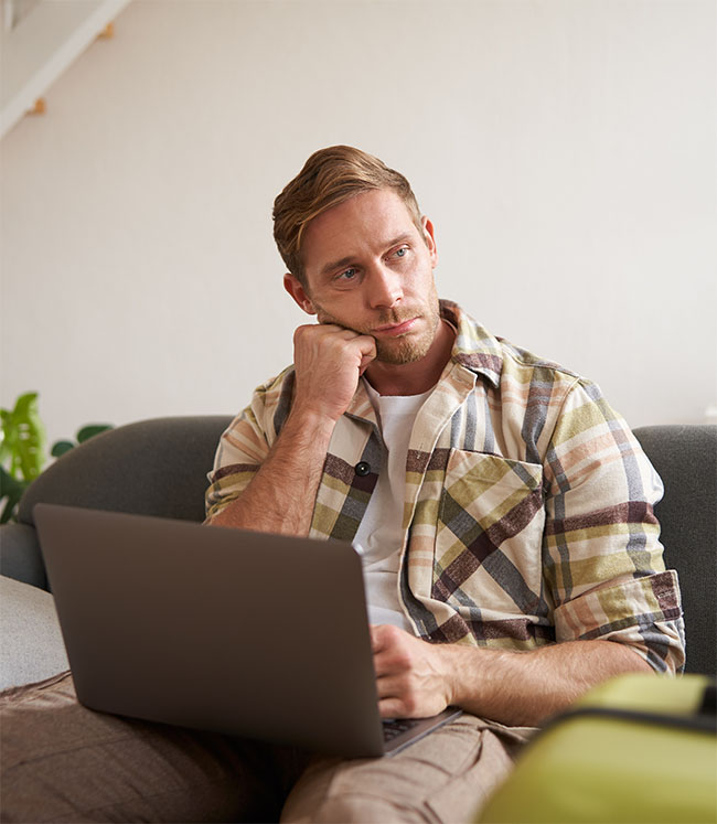 Portrait of upset young man, boyfriend plans holiday trip, has two plane tickets abroad for travelling on holiday, works on laptop