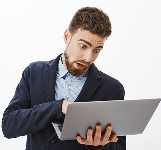 Man going crazy, being in rush working on project. Anxious troubled good-looking male with beard in suit holding laptop looking at computer screen, posing concerned and focused against grey wall